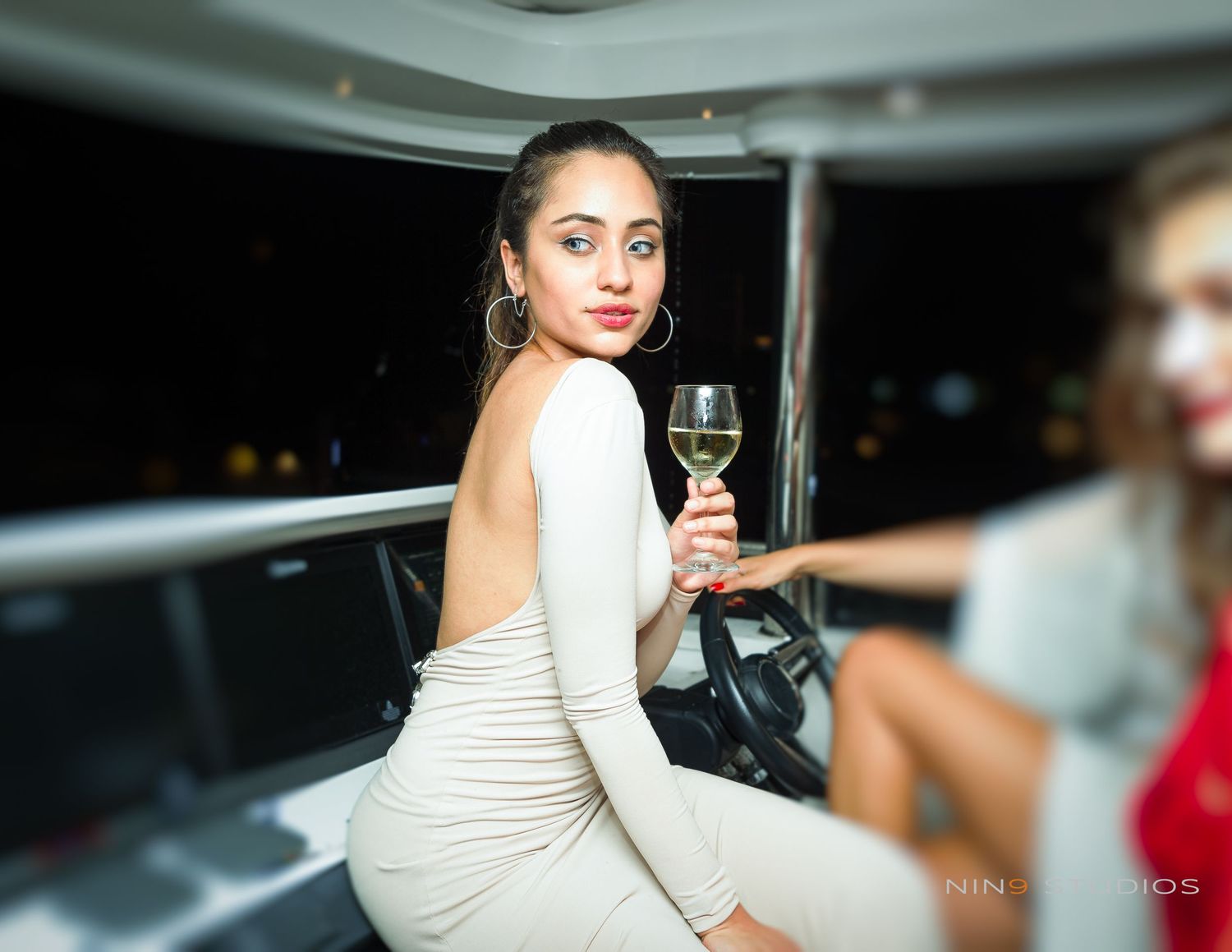 Woman in white backless dress holding wine glass poses elegantly at an upscale evening event.