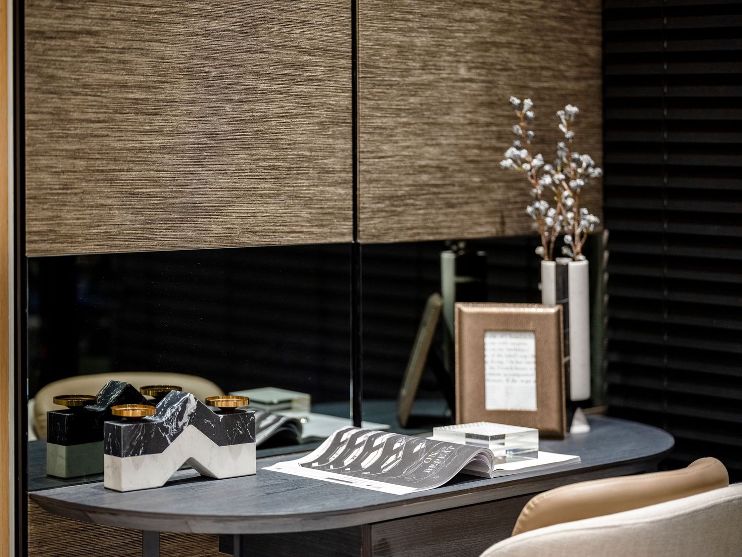 Elegant desk with decorative objects, framed photo, and floral vase against textured wall panels.