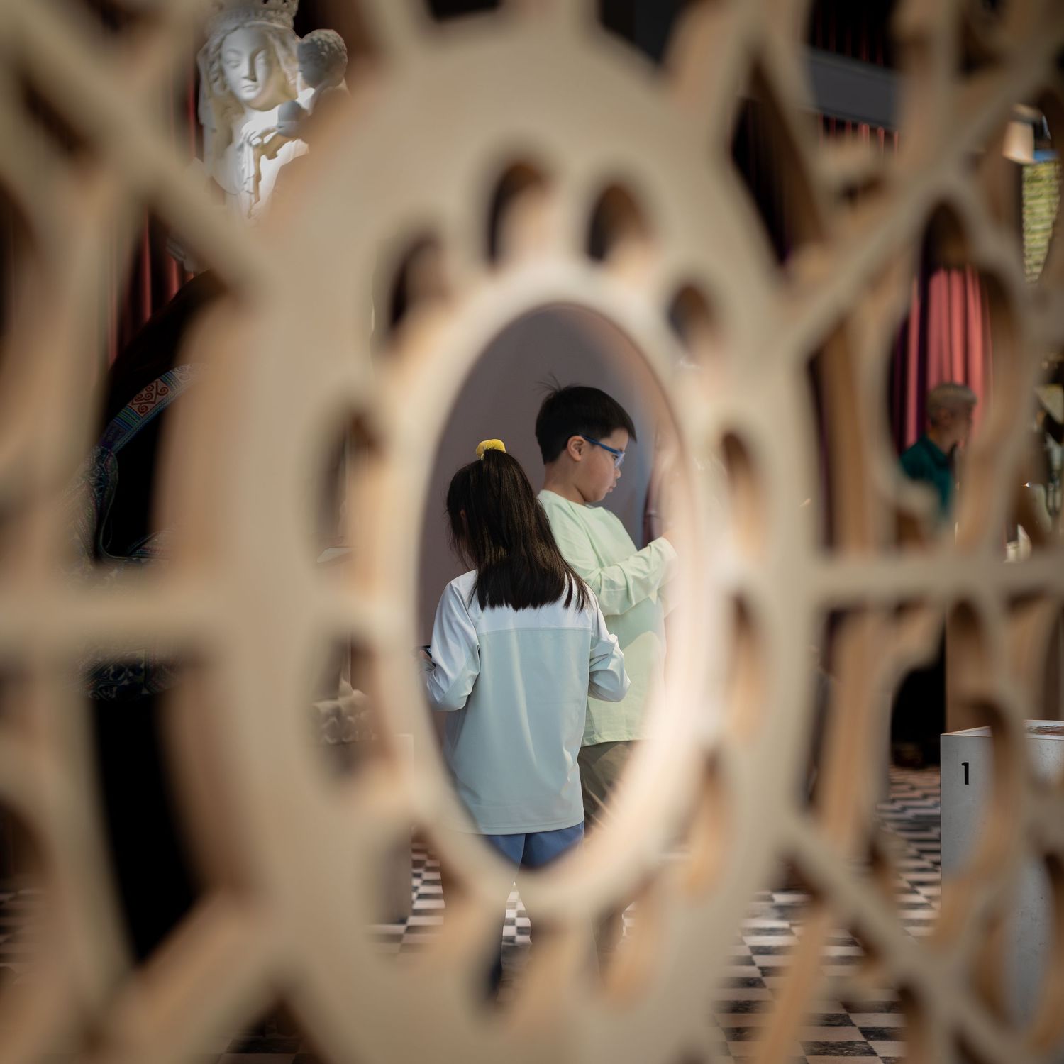 Two children viewed through decorative lattice screen in an art installation.
