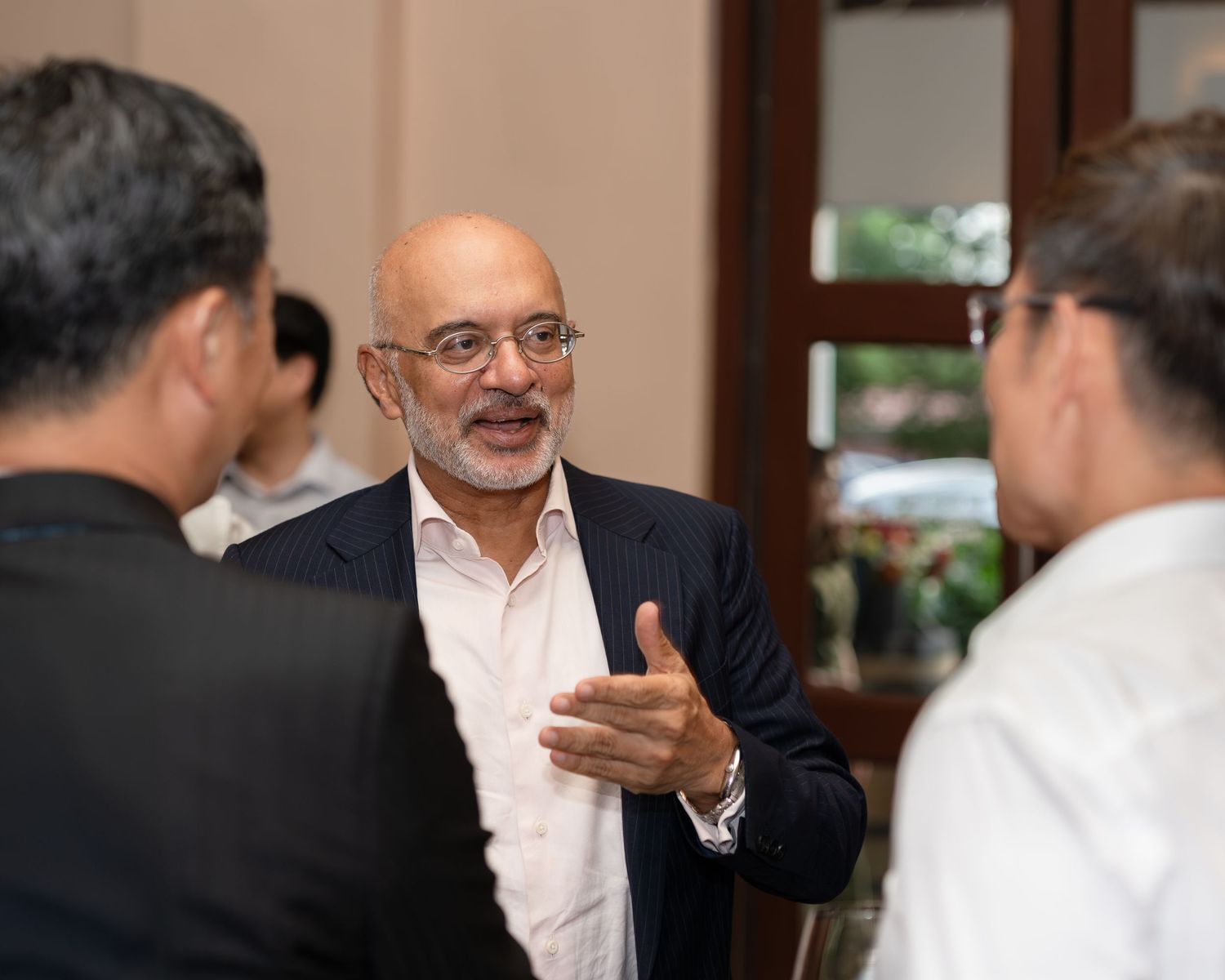 Business professional in dark blazer engages in animated conversation with colleagues at networking event.