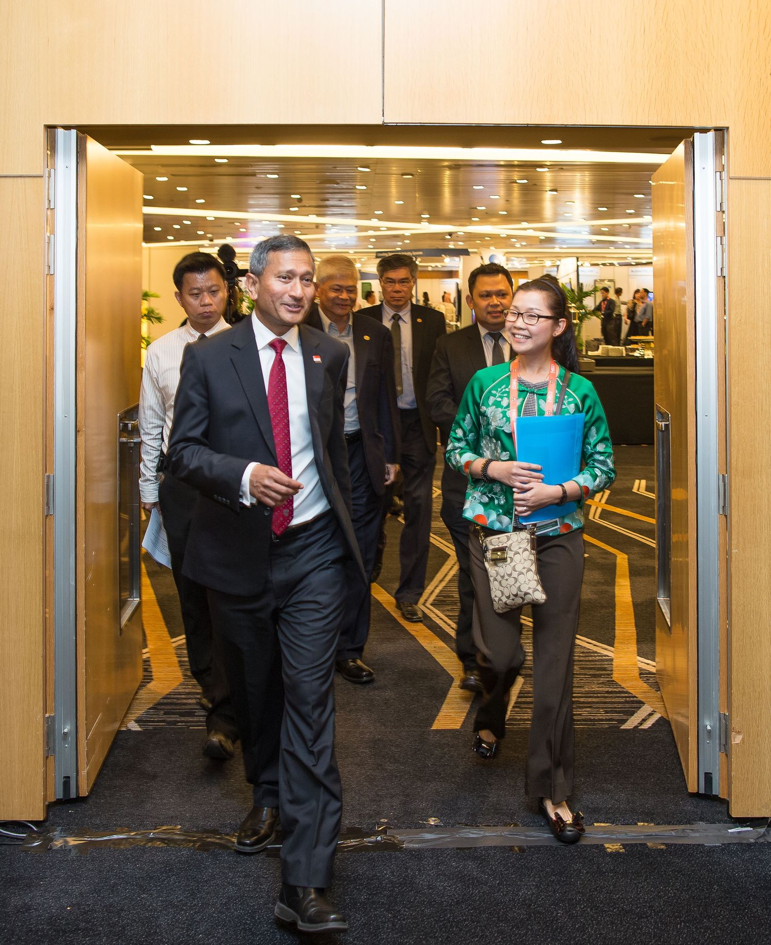 Group of professionals walking through modern building entrance led by man in dark suit.