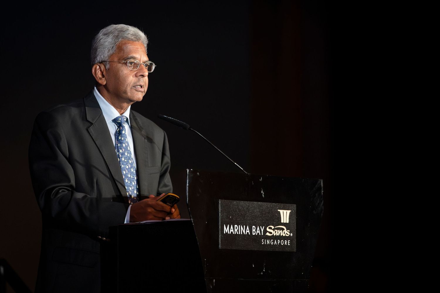 Indian businessman delivers speech at Marina Bay Sands Singapore podium in formal attire.