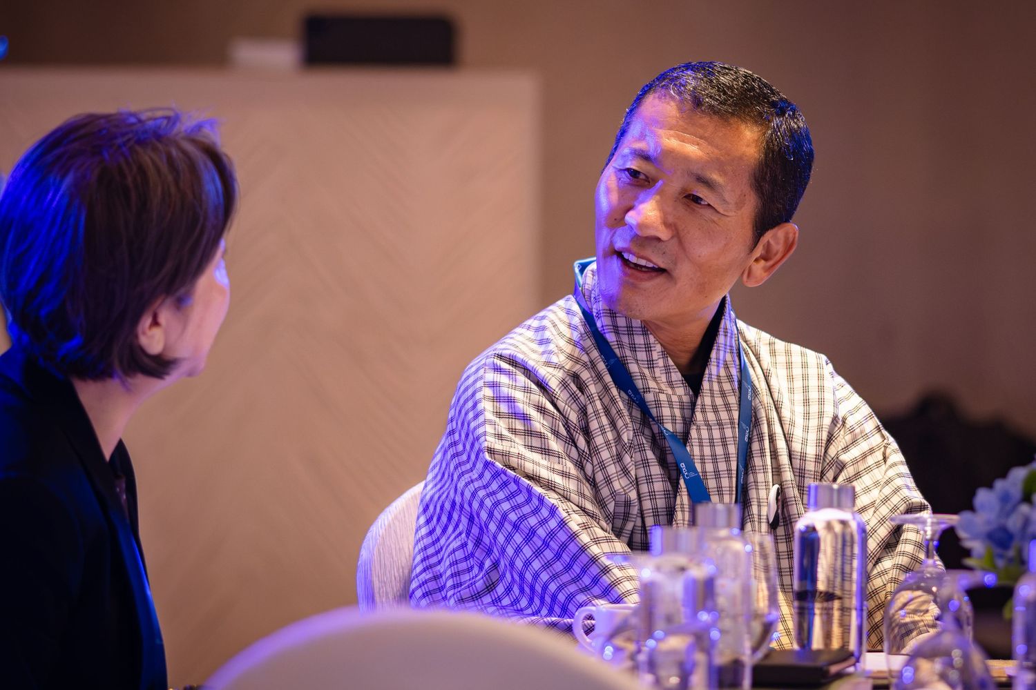 Man in traditional checkered attire with lanyard engages in conversation at a conference.