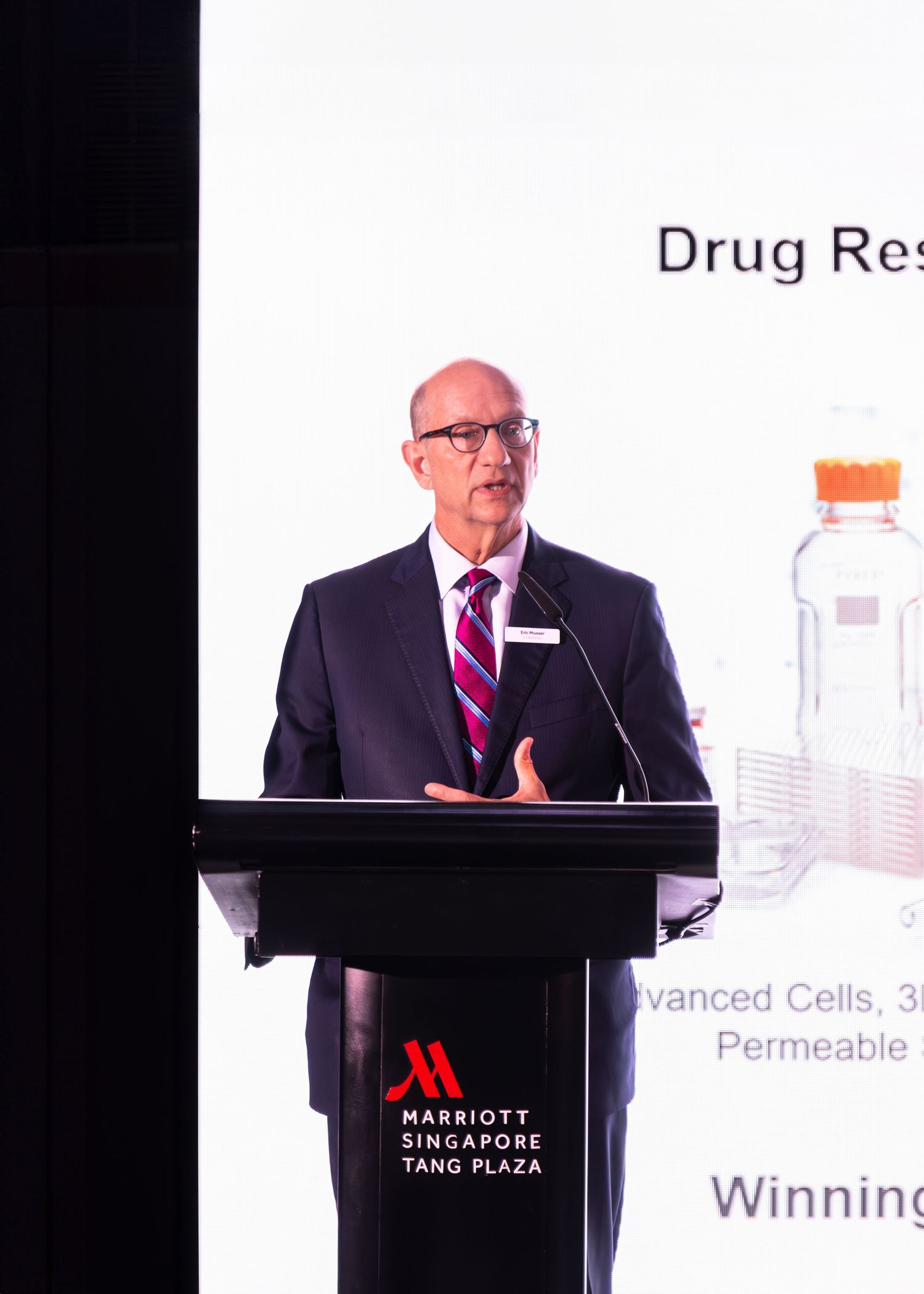 Executive delivers speech at podium during Corning drug research presentation at Marriott Singapore Tang Plaza.