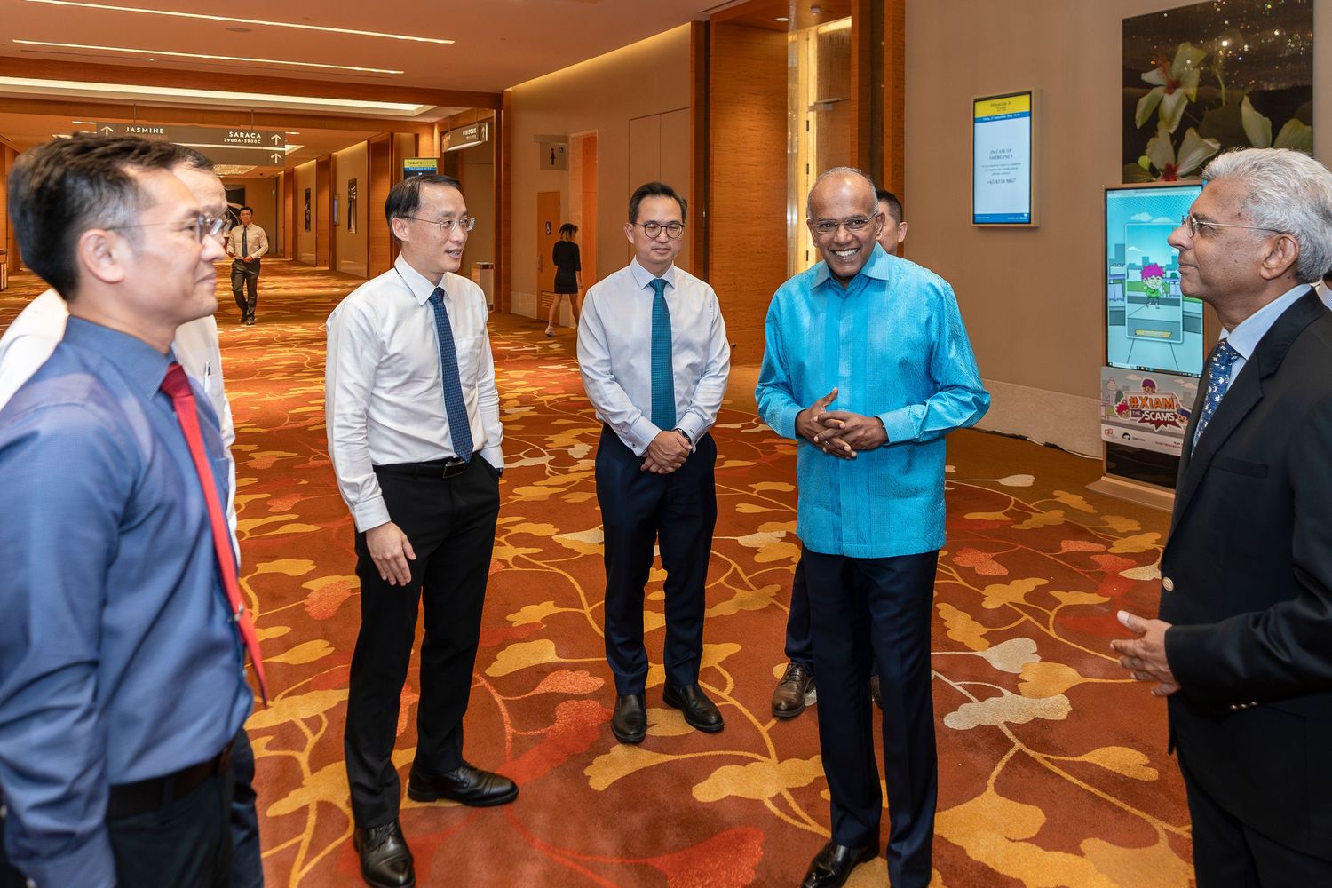 Five professionals in formal attire engaged in conversation in an elegant hotel corridor.