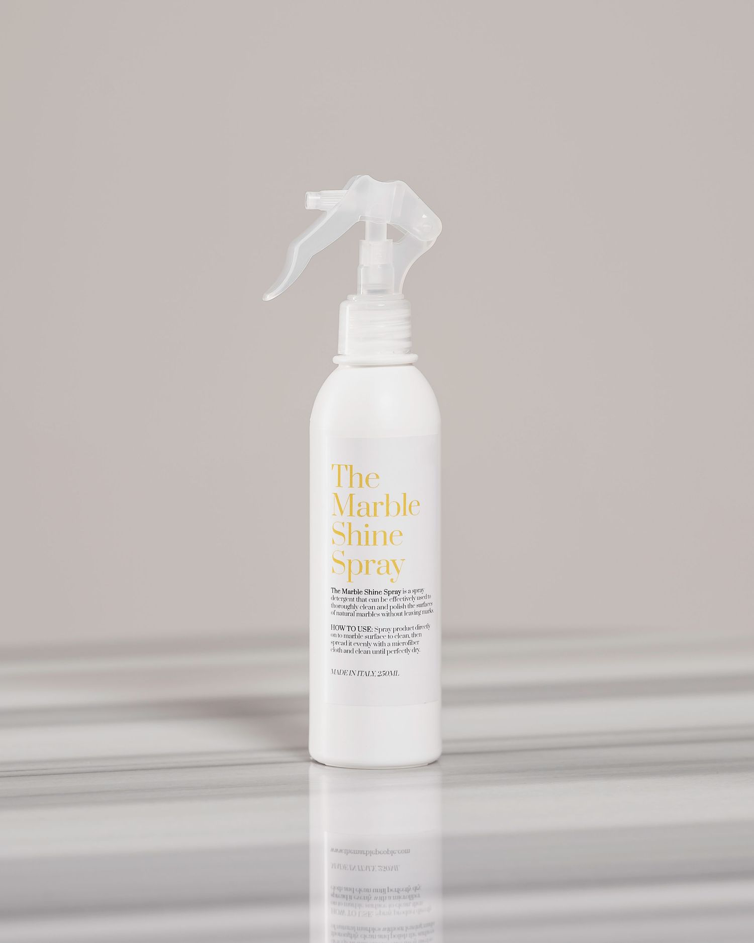 The Marble Shine Spray white trigger spray bottle on reflective surface with neutral background.