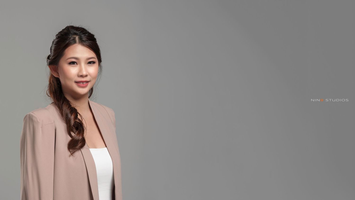 Professional Asian woman in pink blazer smiling confidently against a gray background.