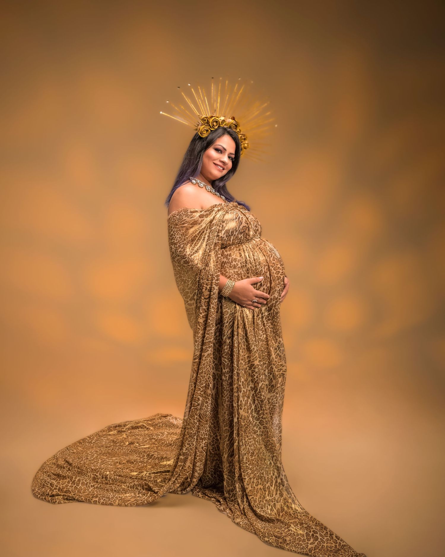 Pregnant woman in gold sequin gown and crown poses regally in elegant maternity portrait.