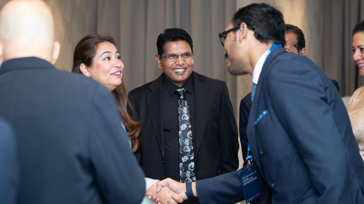 Group of professionals in formal wear exchanging handshakes and greetings at a networking event.