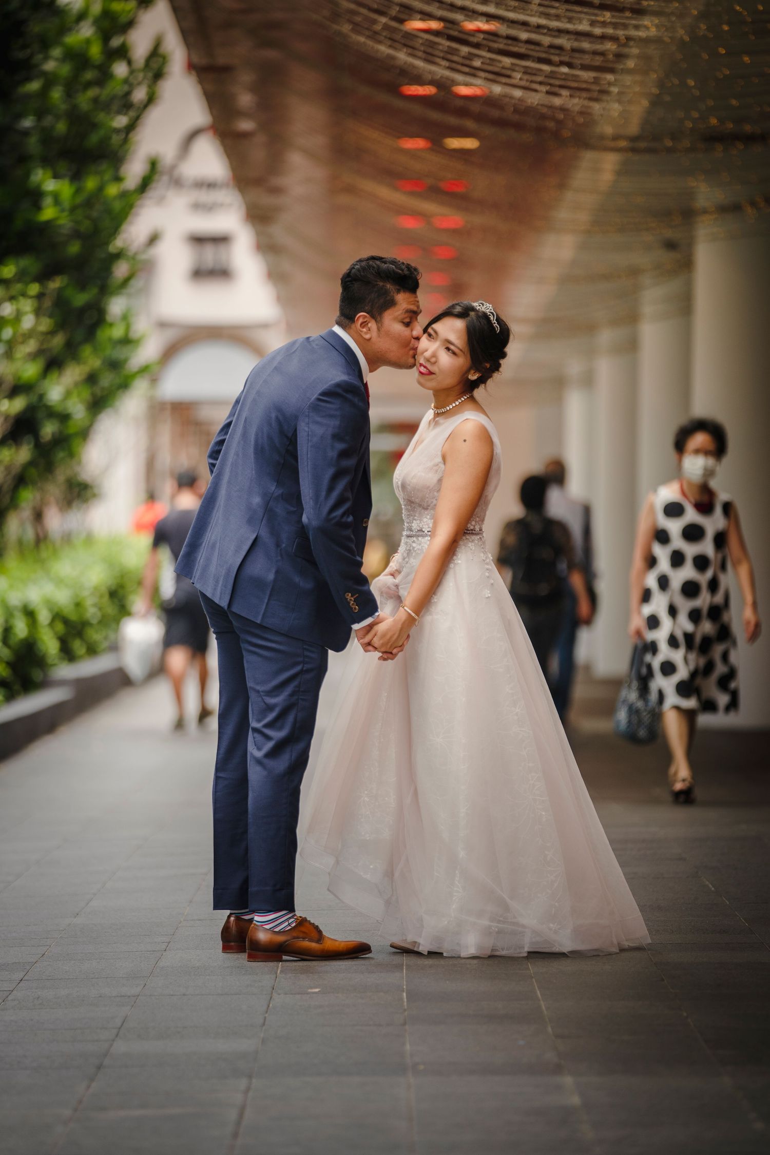A couple shares a romantic moment in a wedding photo, bride in white gown and groom in navy suit holding hands outdoors.