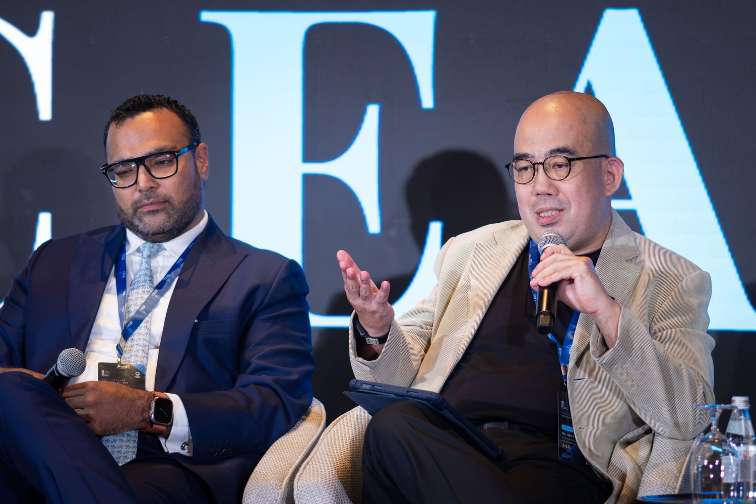 Two male panelists engaged in discussion at a professional conference event.