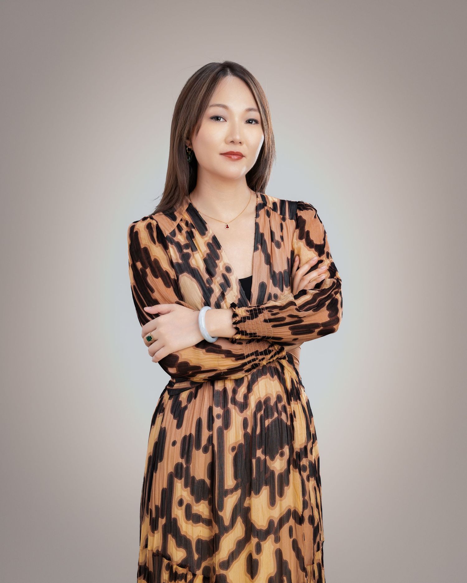 Woman in leopard print dress with arms crossed posing elegantly against a neutral gradient background.