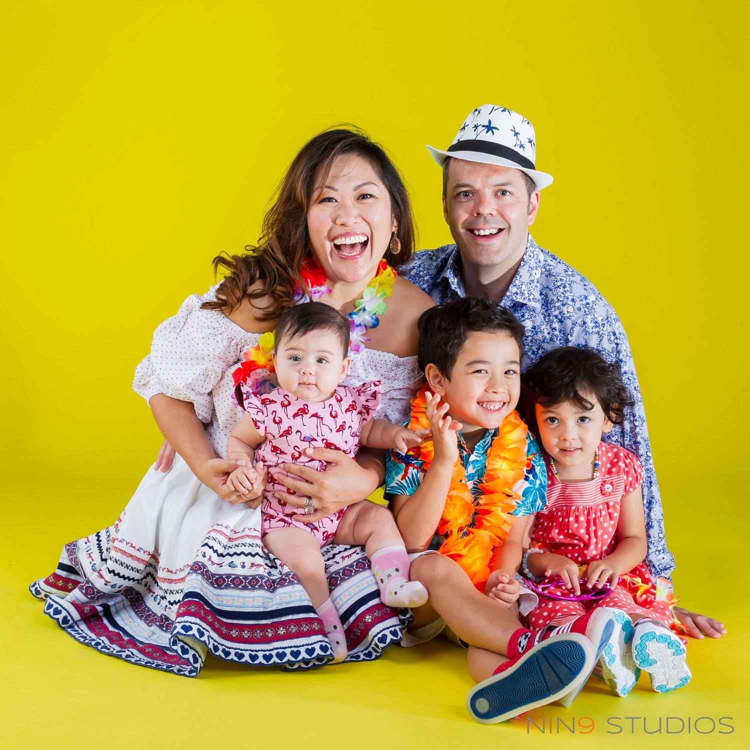 Happy family of five posing together in colorful tropical outfits against a bright yellow background.