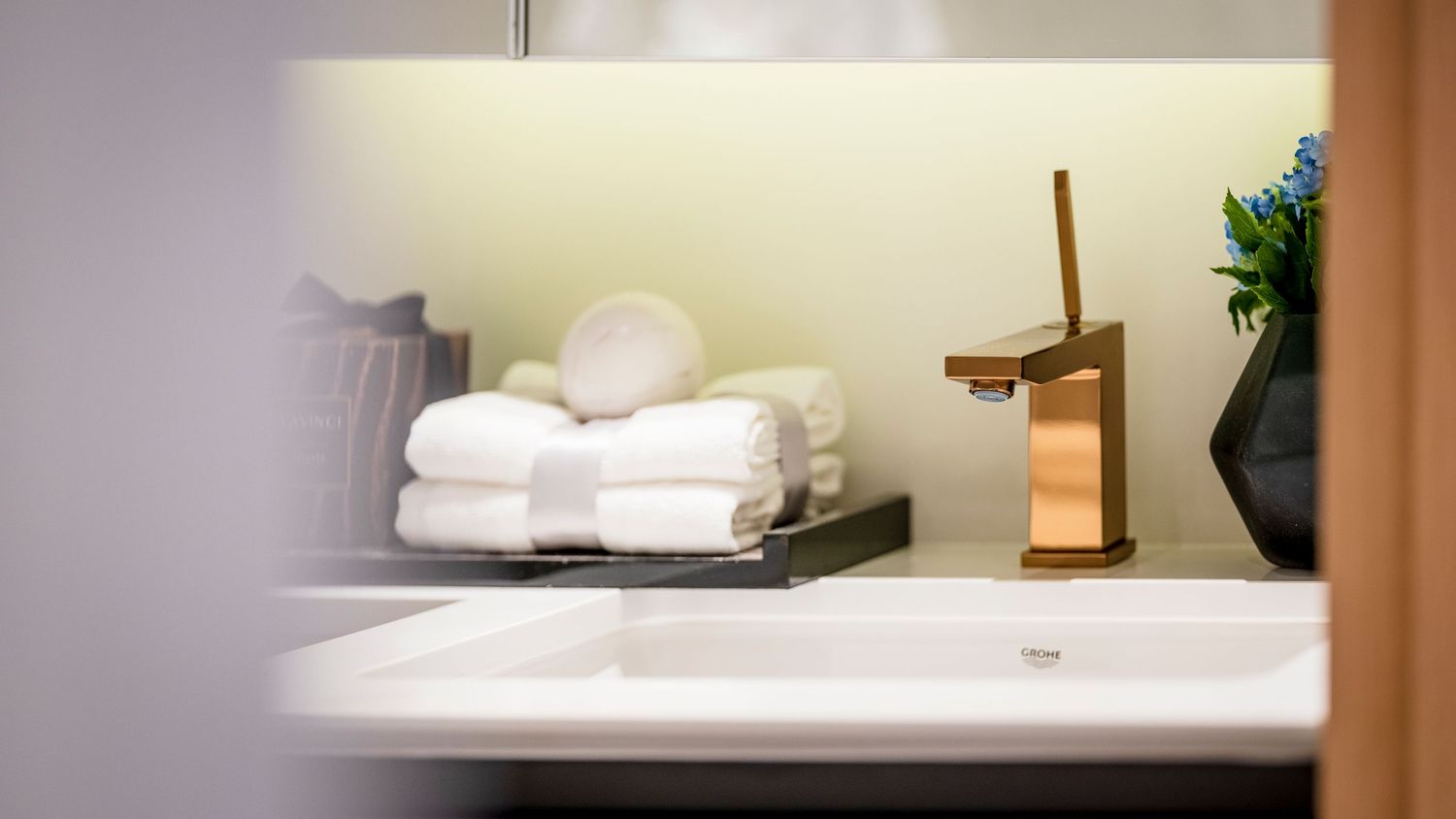 Elegant bathroom vanity with gold faucet, white sink, and neatly folded white towels on a shelf.