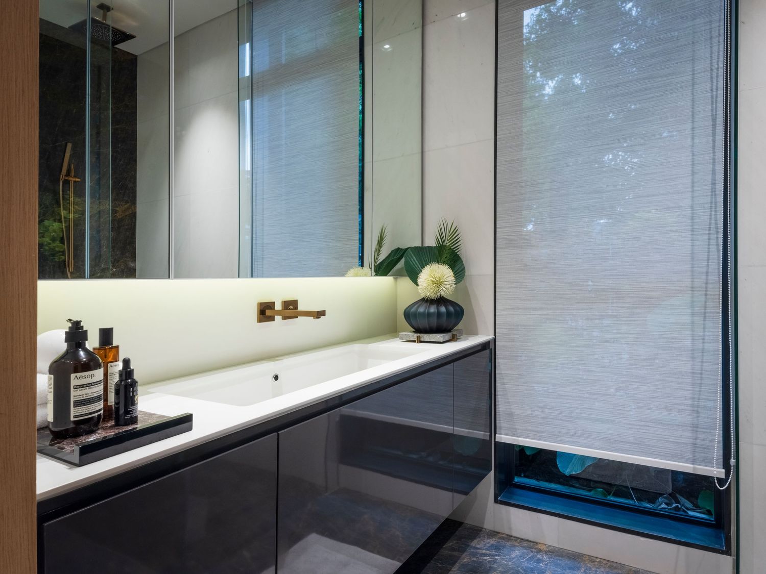 Sleek modern bathroom vanity with white basin, dark cabinets, mirror, and bamboo blind window.
