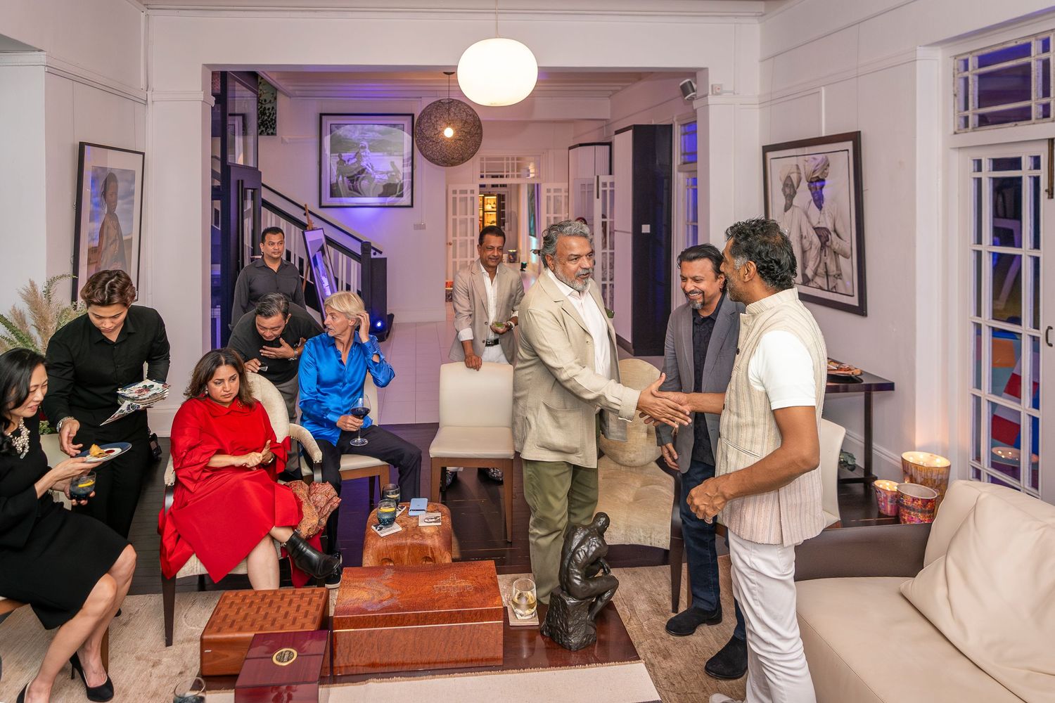 Guests mingling and shaking hands at an elegant indoor social gathering in a decorated home.