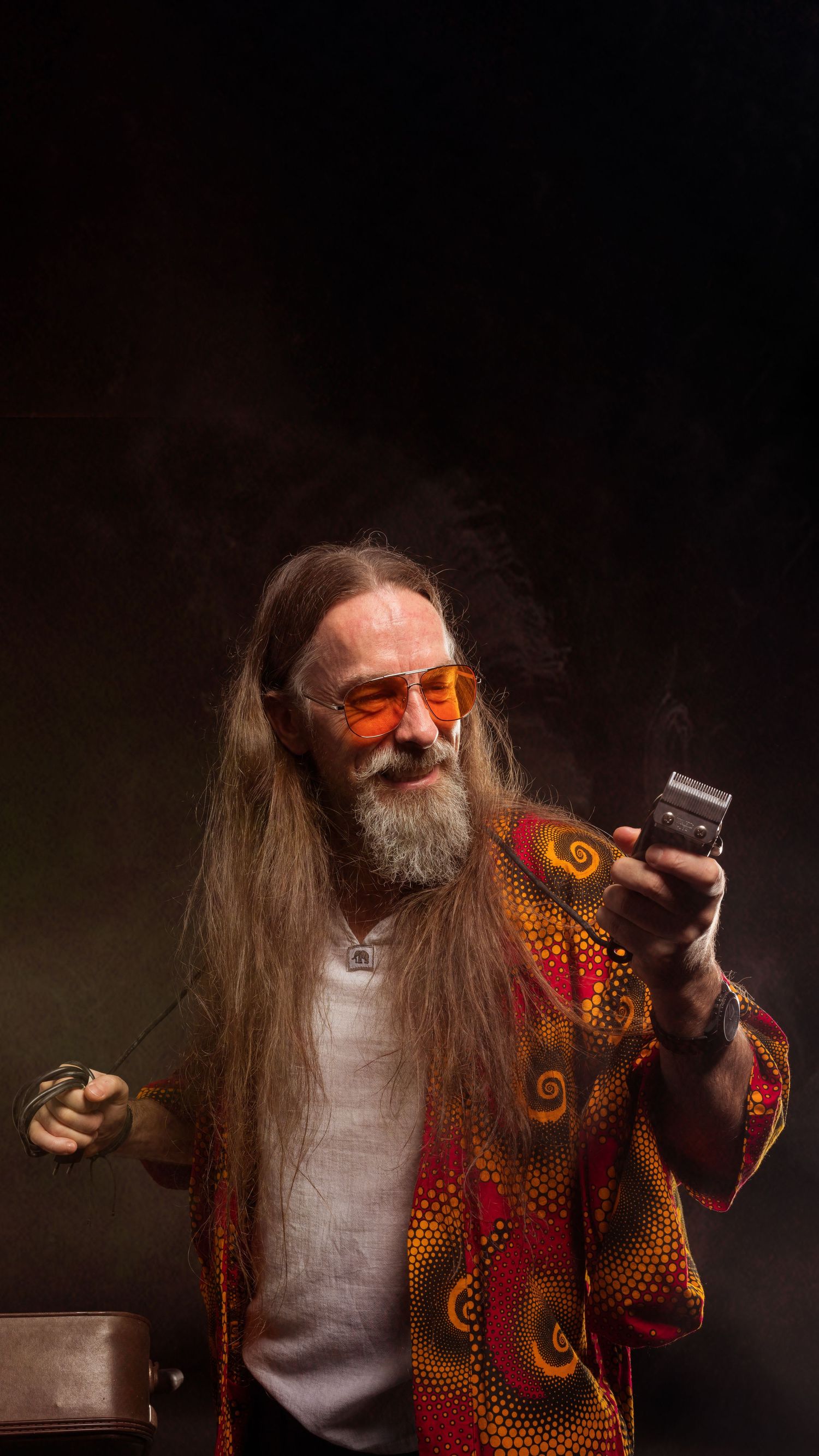 Long-haired bearded man in colorful bohemian shirt holding lighter with smoke on dark background.