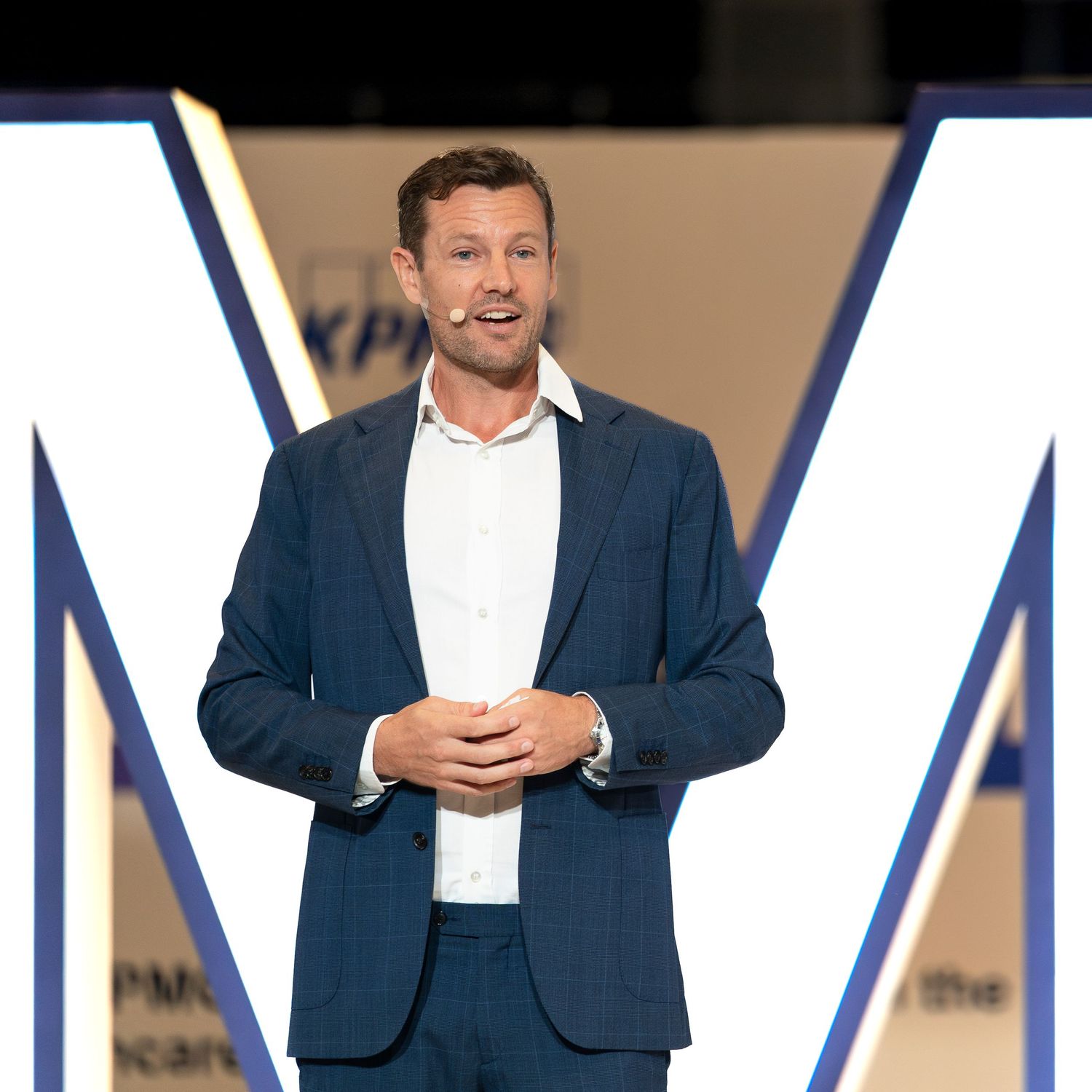 Professional speaker presenting on stage at corporate conference in blue suit.