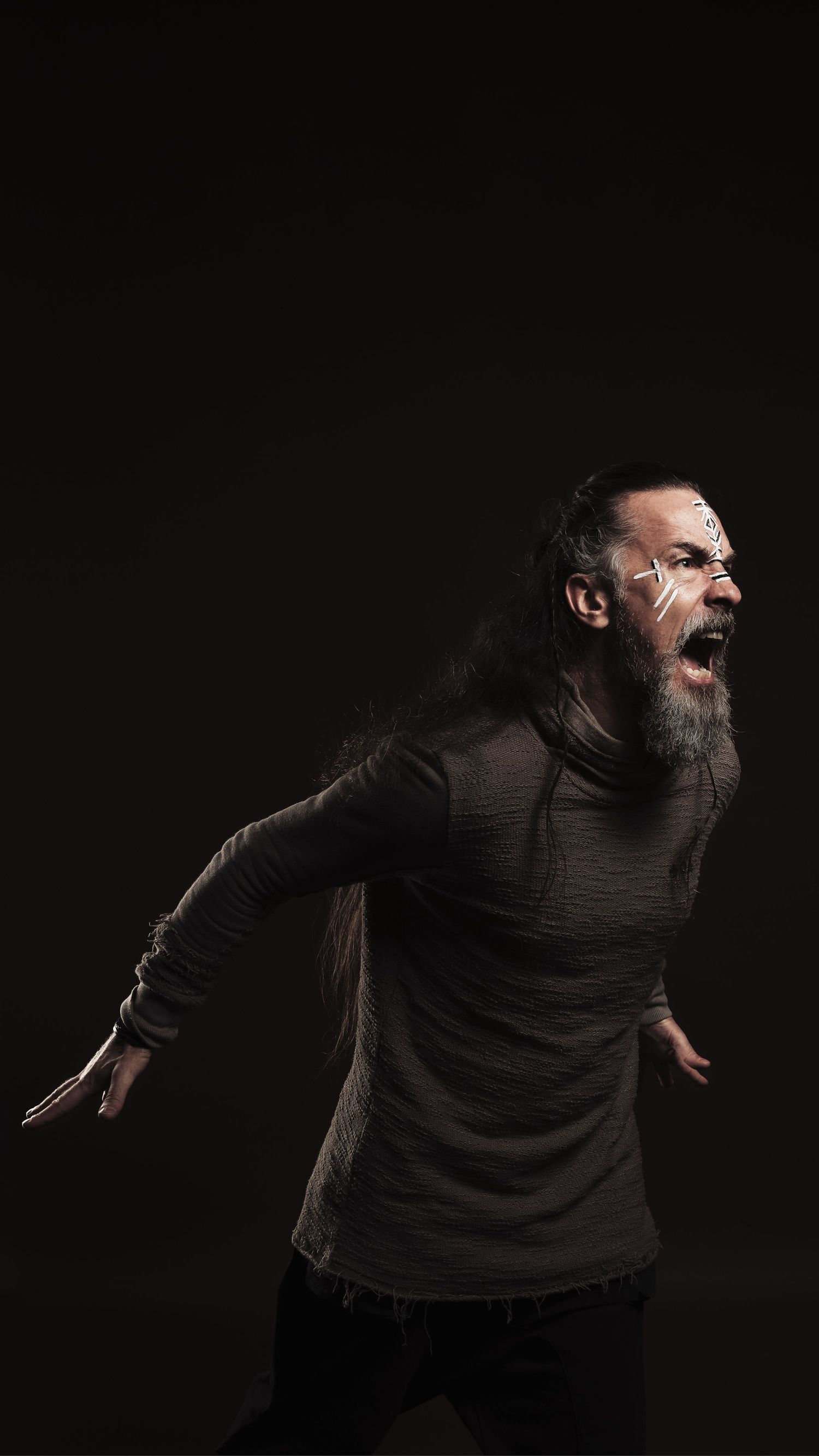 Intense bearded Viking warrior screaming in dramatic dark studio lighting with face paint and long hair.