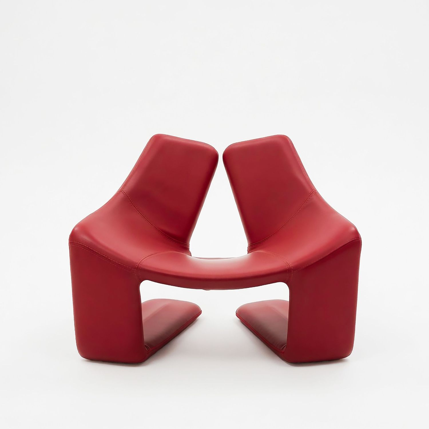 Modern red leather double chair with curved sculptural design and split back, minimalist contemporary furniture piece.