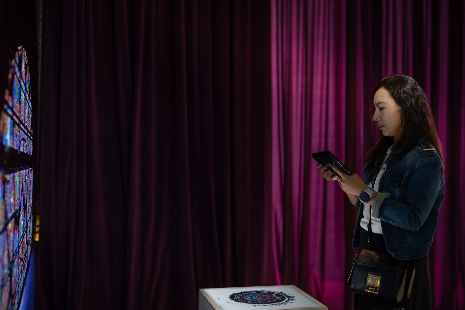 Woman using smartphone to view artwork display near purple curtain at museum exhibit.