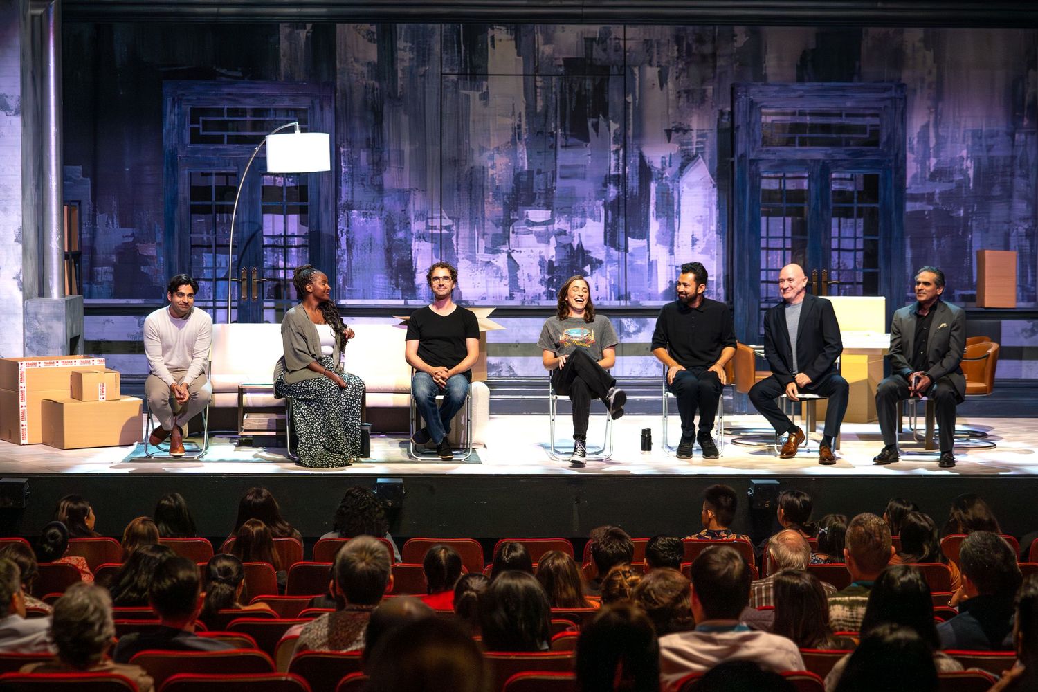 Seven panelists seated on stage during a theater discussion event before an audience.