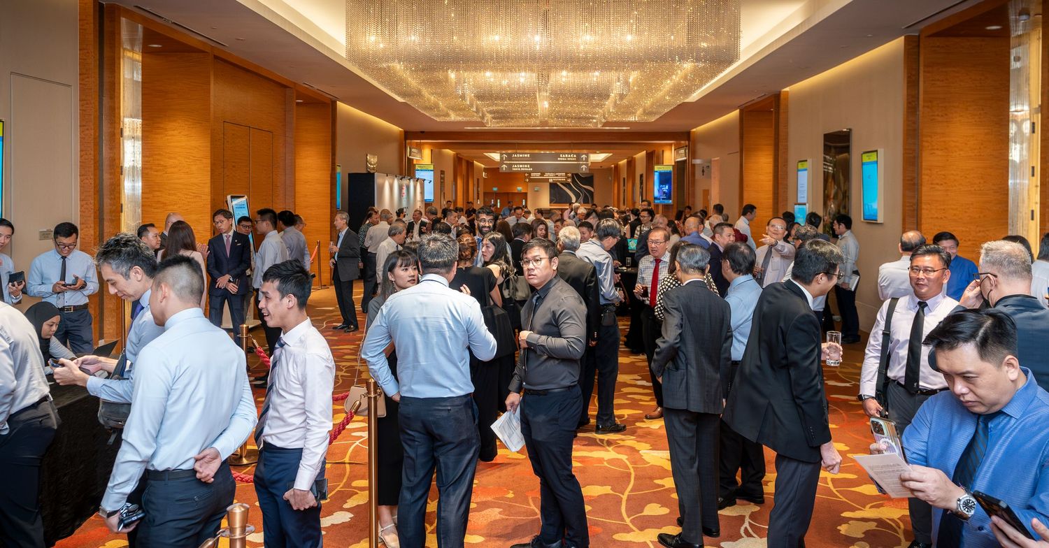 Large crowd of business professionals networking in a modern hotel ballroom corridor at a conference.