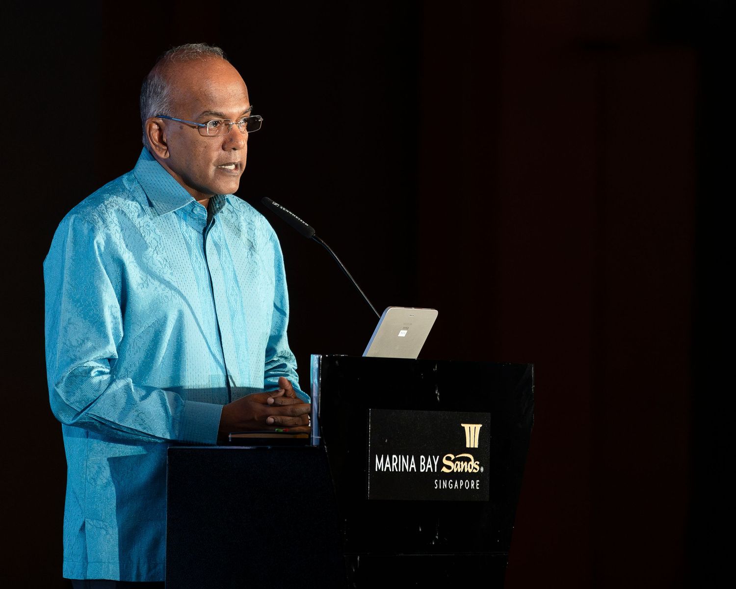 Man in blue shirt delivers speech at podium during Marina Bay Sands Singapore corporate event.