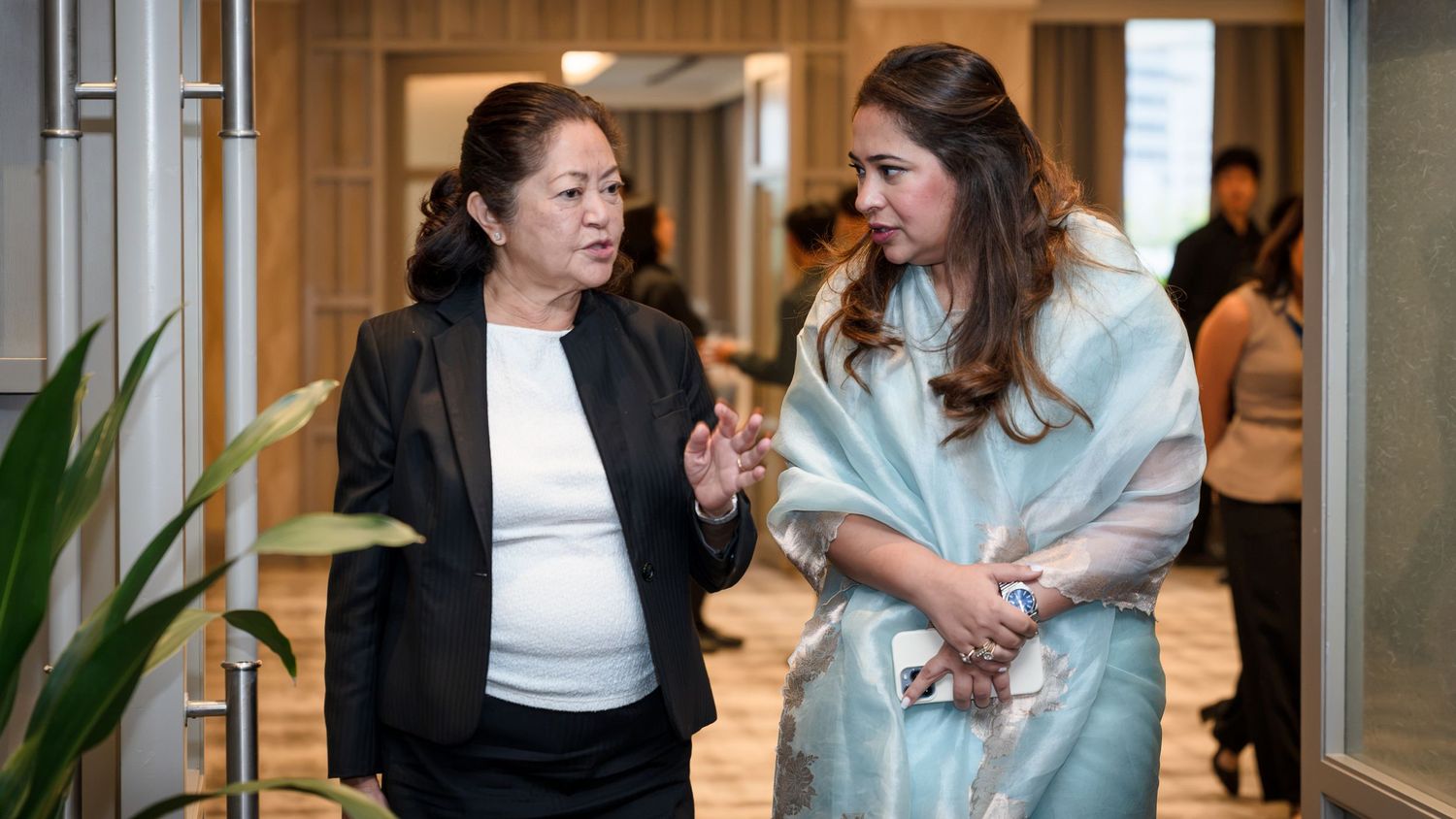 Two professional women in business attire engaged in conversation at a modern corporate event venue.