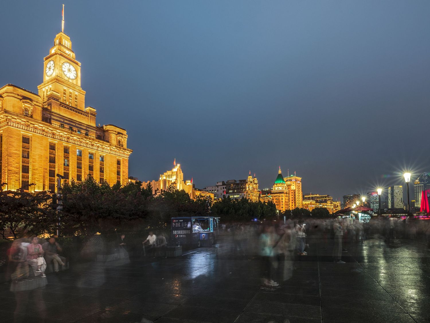 The illuminated Bund waterfront in Shanghai at dusk, featuring the iconic Custom House clock tower and historic colonial buildings.