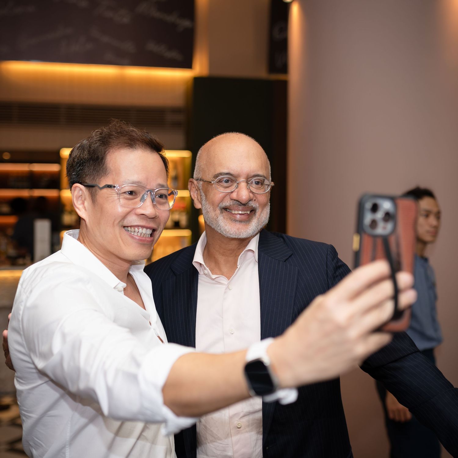 Two smiling men taking a selfie together at an indoor social gathering or corporate event.