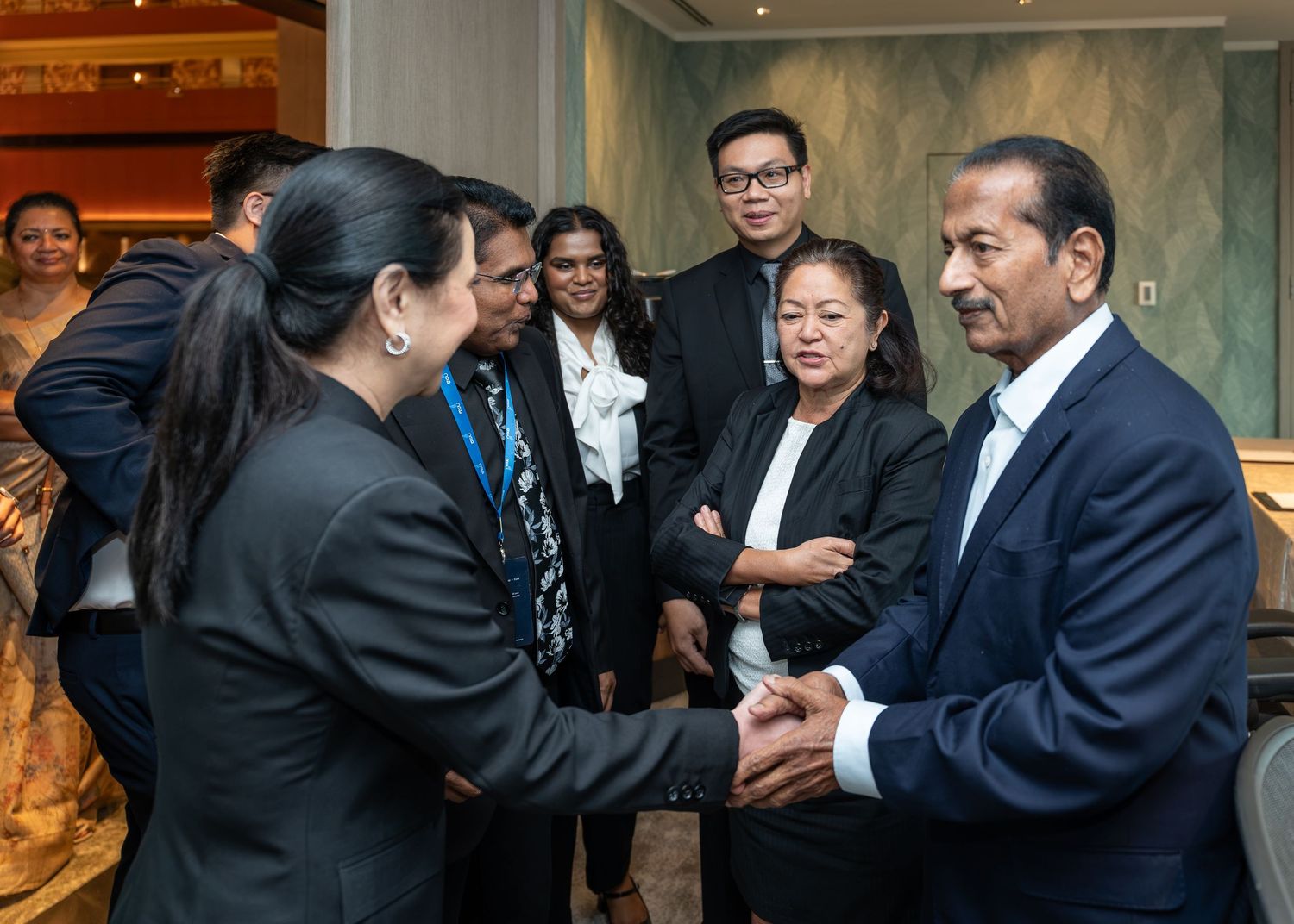 Group of professionals networking at a formal event, shaking hands and engaging in conversation in an elegant venue.