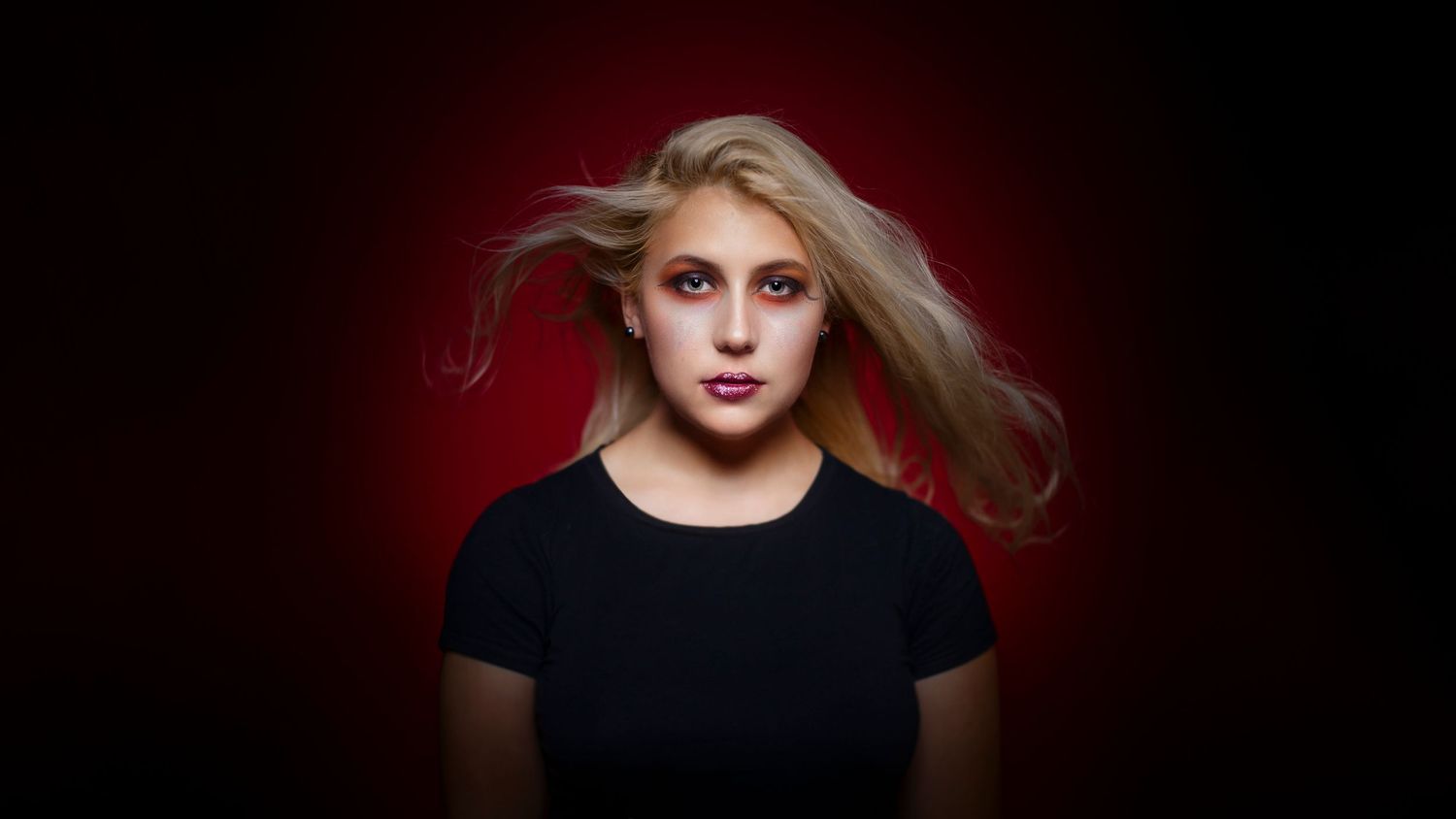 Young blonde woman in black top with flowing hair against dramatic red and dark background.