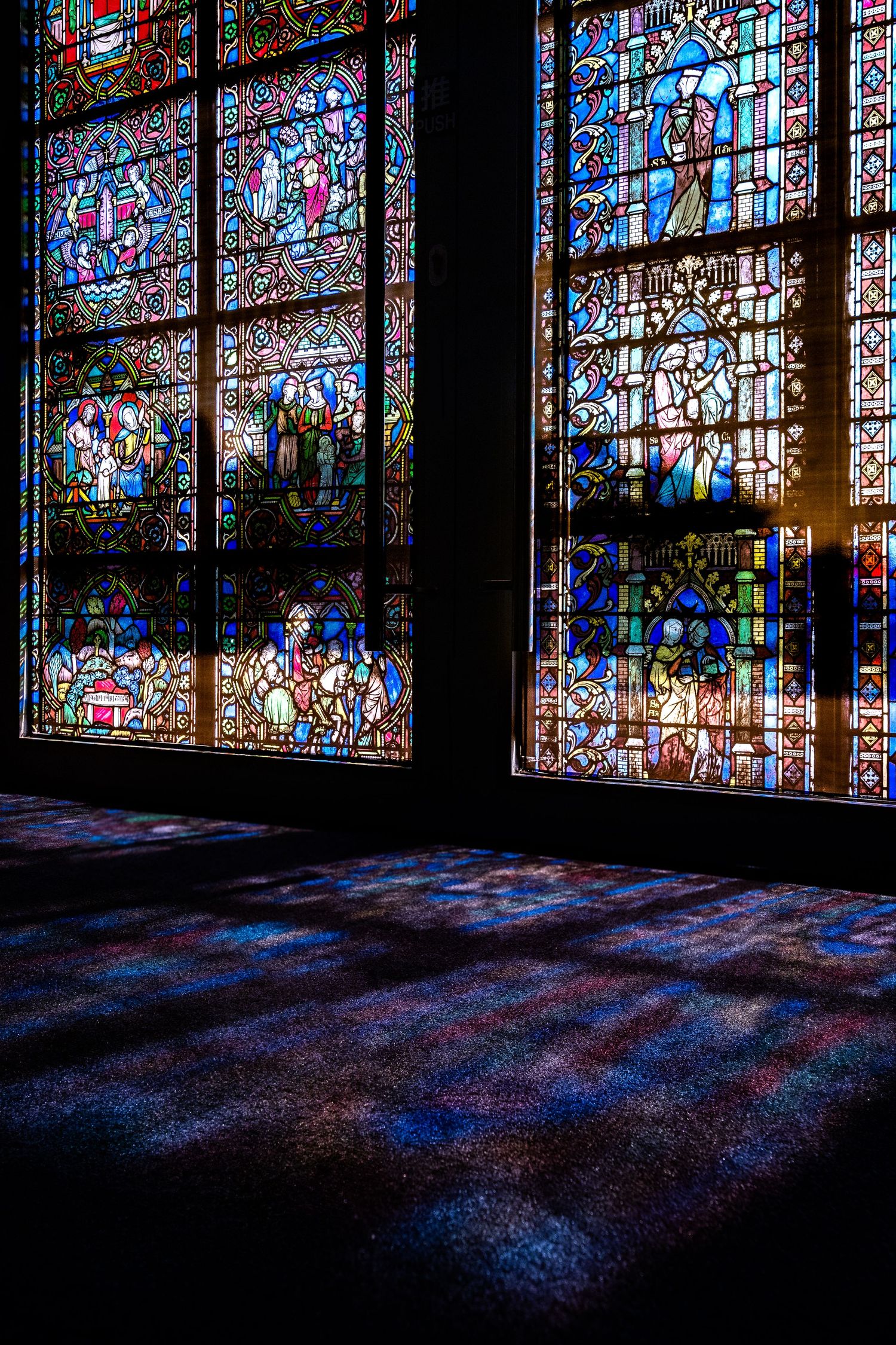 Stunning stained glass cathedral windows casting colorful light patterns on the dark floor below.