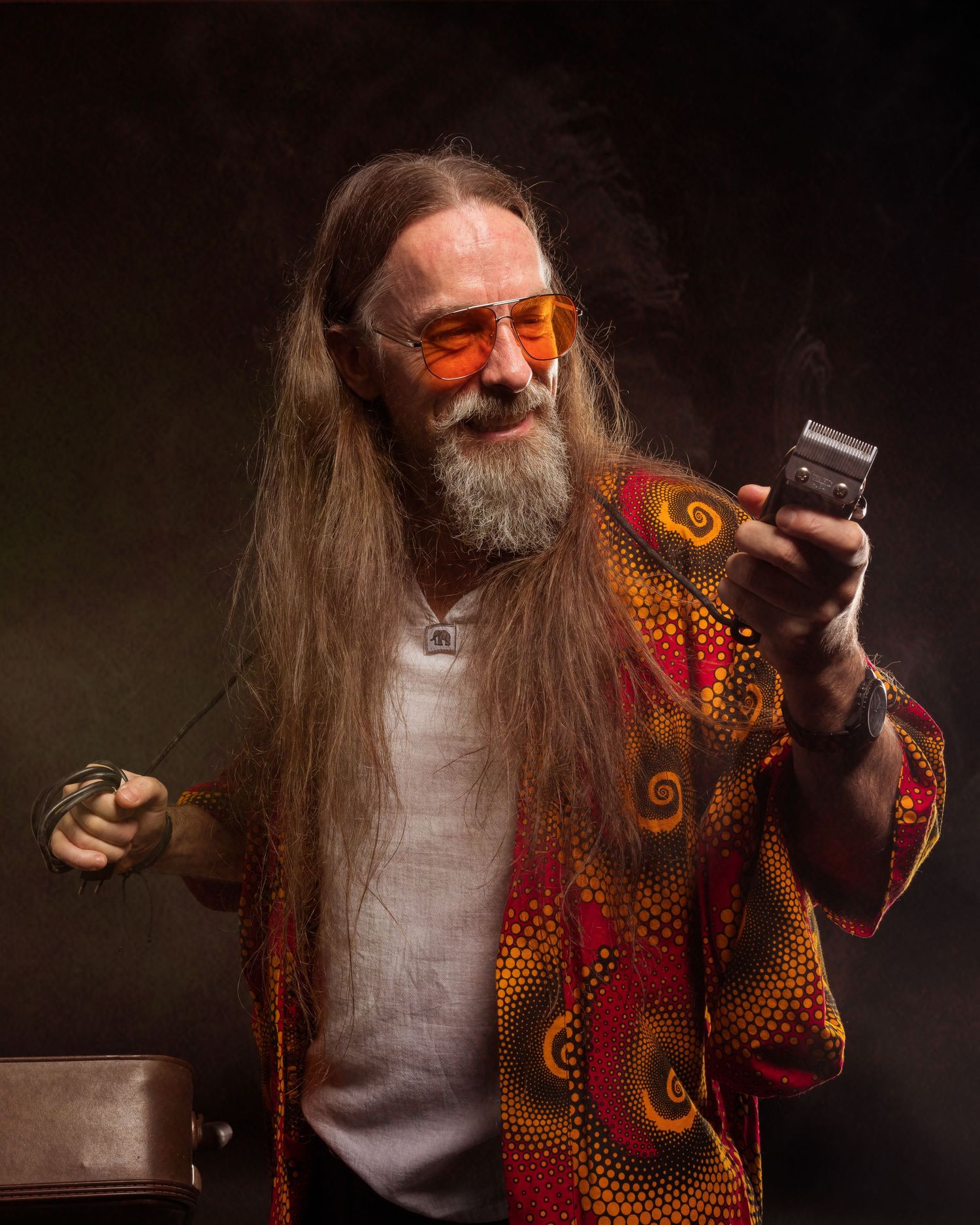 Elderly man with long gray hair, beard, orange tinted sunglasses, colorful psychedelic shirt, holding a flip phone.
