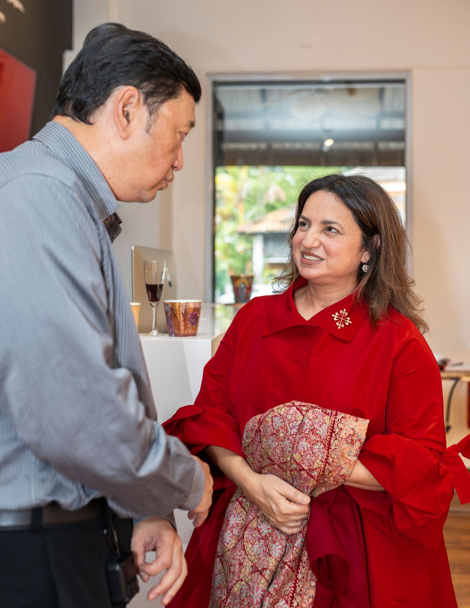 Man and woman in red outfit engaged in conversation at an art gallery reception with decorative items displayed.