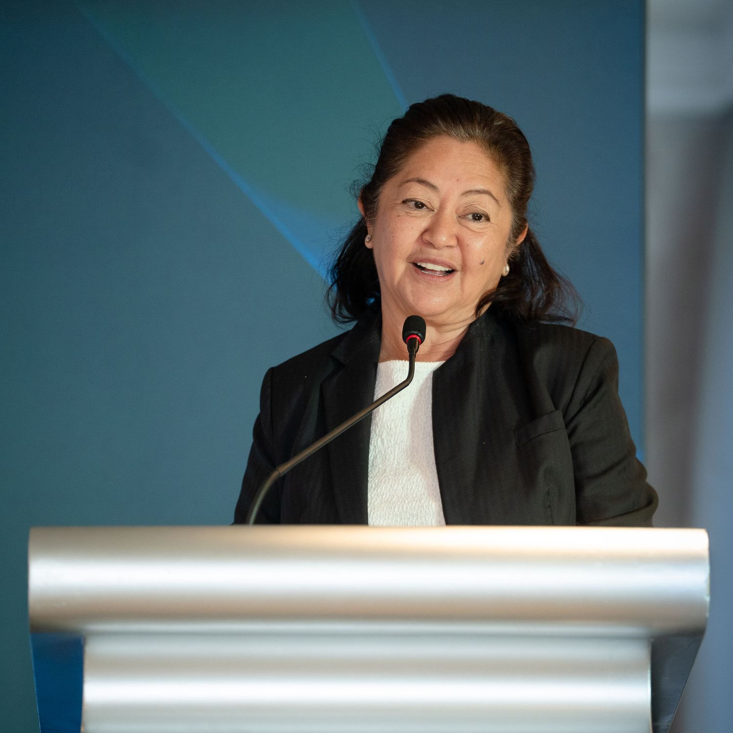 Woman in black blazer speaking at podium during professional conference event.