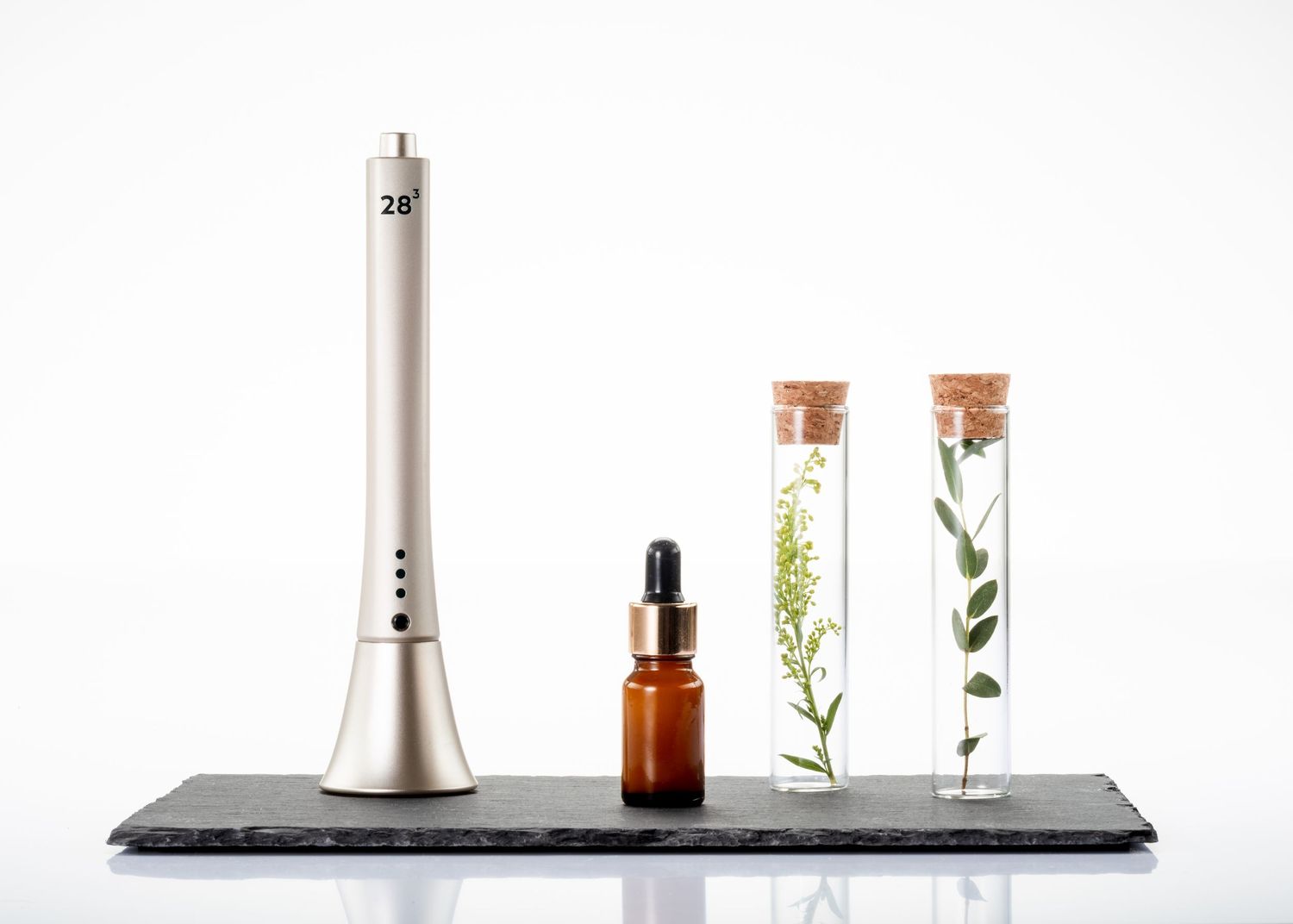 Gold electronic beauty pen displayed with amber dropper bottle and botanical test tubes on slate.