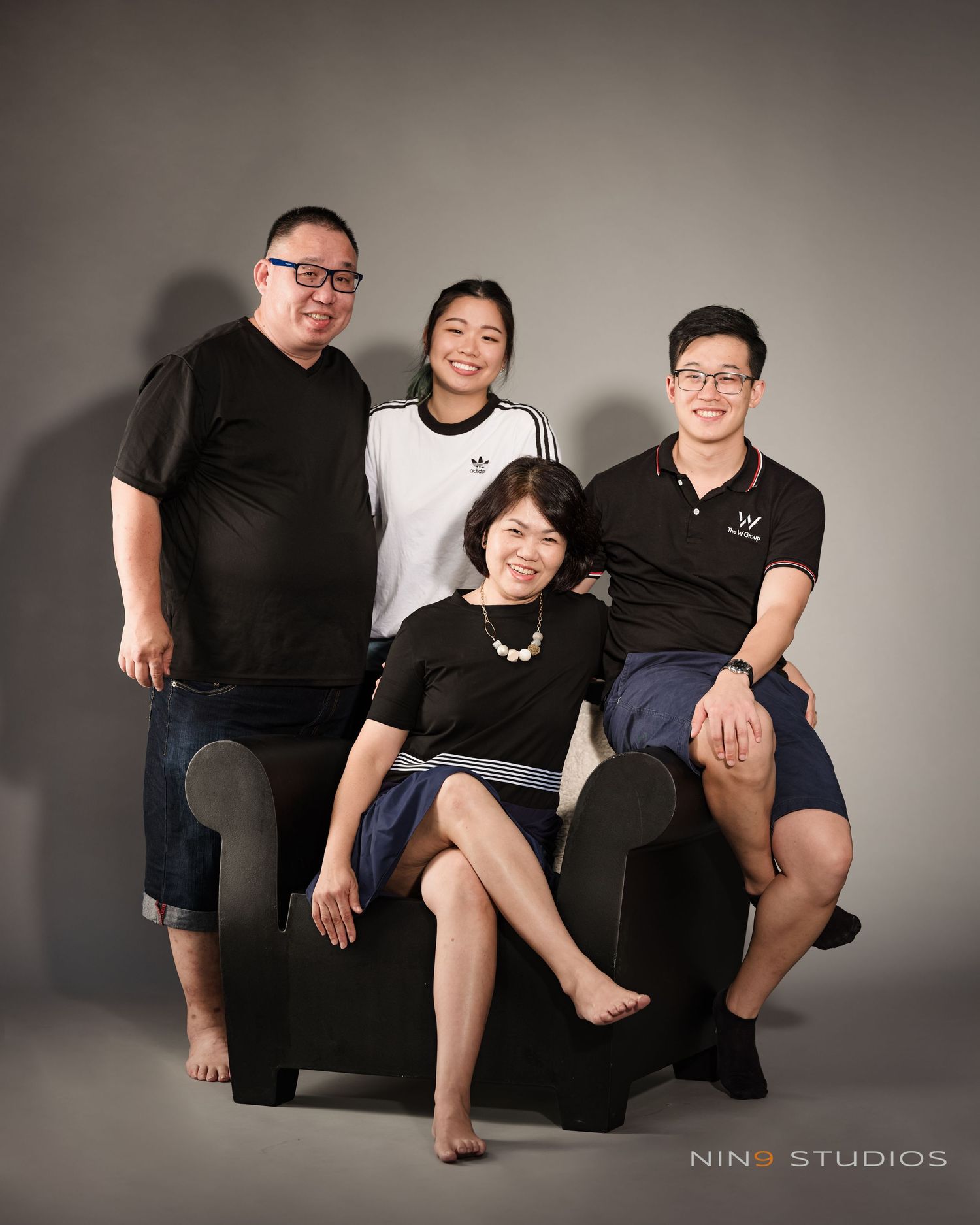 Family of four posing for a professional studio portrait at Ning Studios, seated and standing around a black armchair.