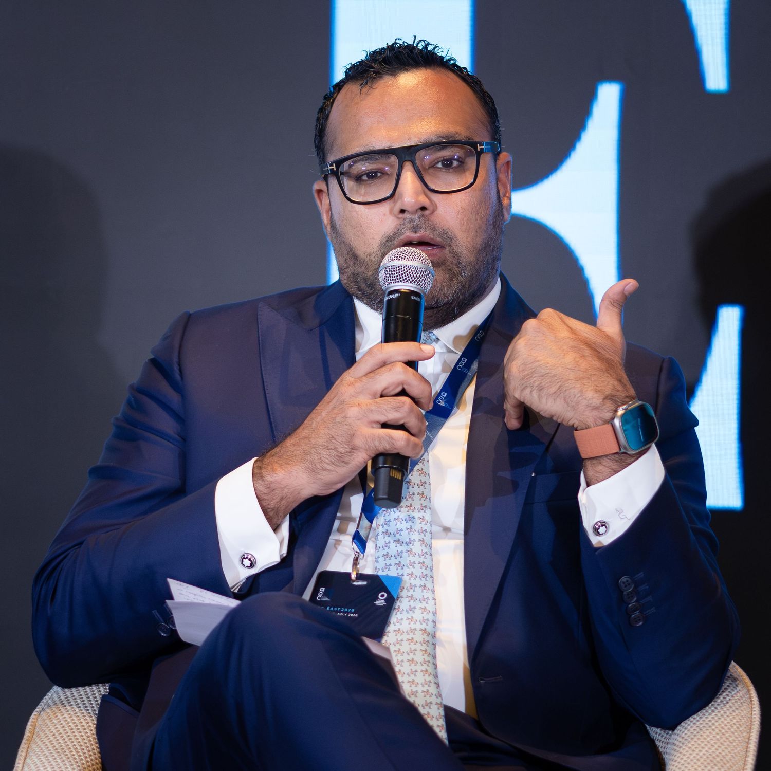 Professional man in navy suit speaking at a conference panel discussion.