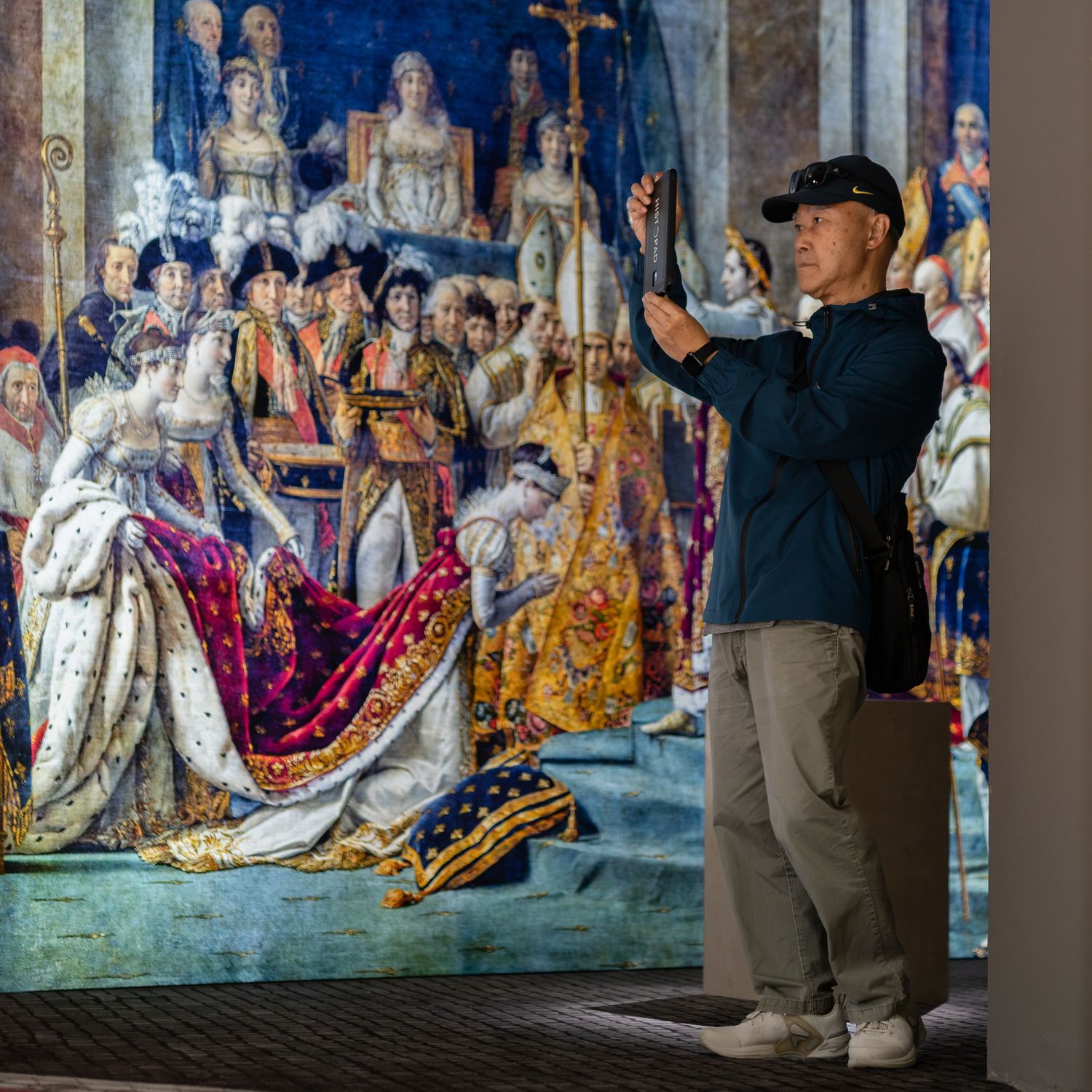 Visitor photographs large Napoleon coronation painting reproduction at a museum or immersive art exhibition.
