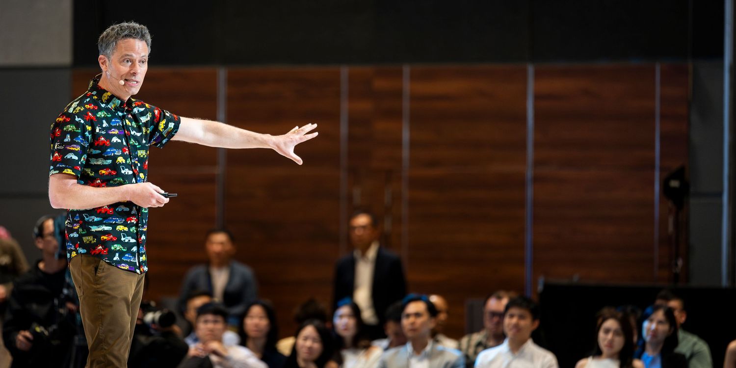 A speaker in a colorful floral shirt gestures to an audience during a presentation event.