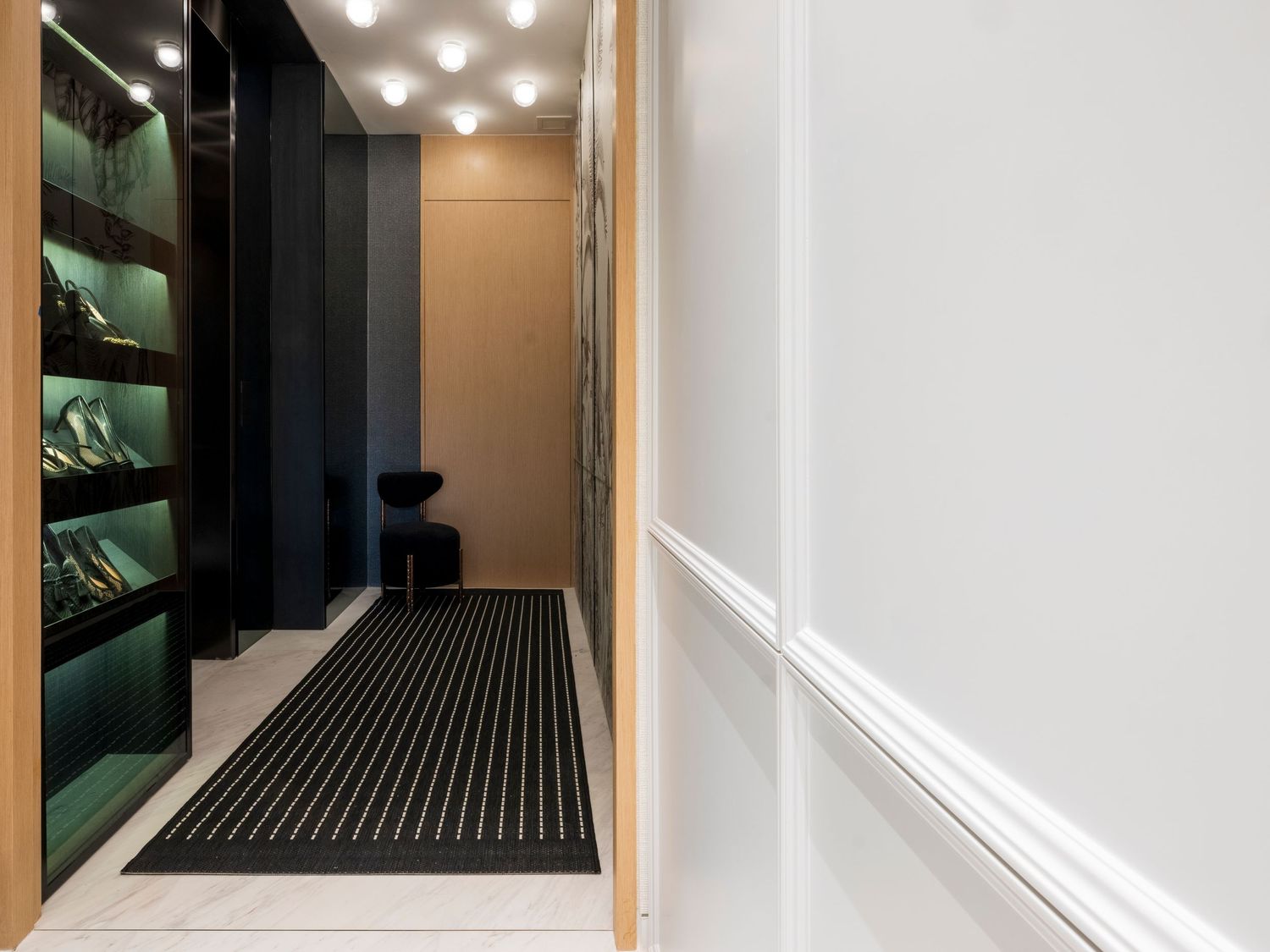 Sleek modern hallway with illuminated green shoe display shelves and striped black floor runner.