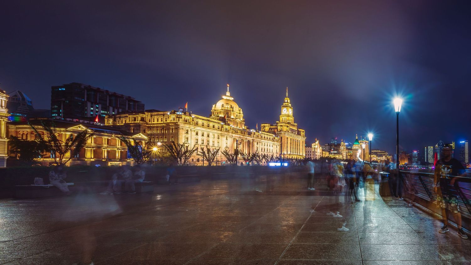 The Bund in Shanghai illuminated at night with historic buildings and busy waterfront promenade under glowing street lamps.