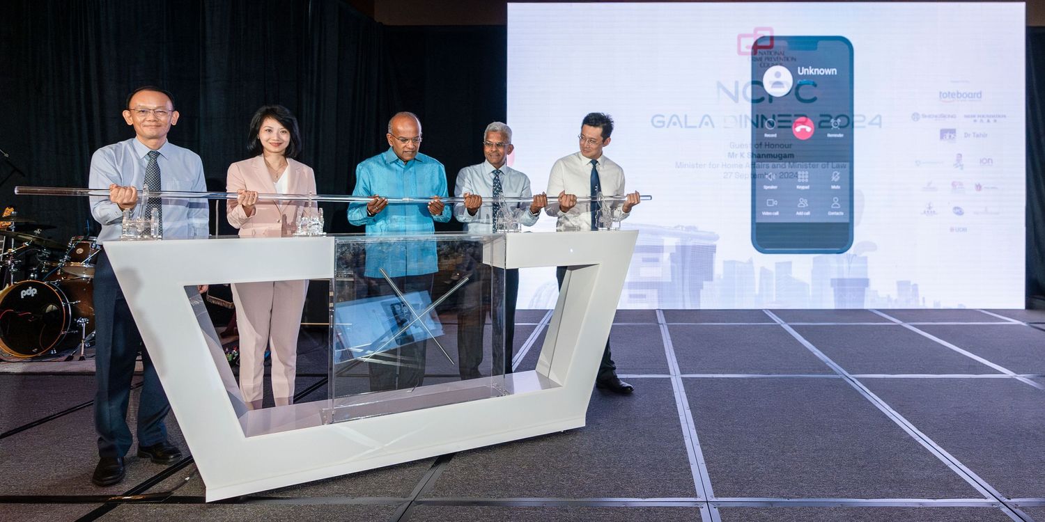Group of professionals launching a mobile app at a formal event with a large screen displaying the app interface.