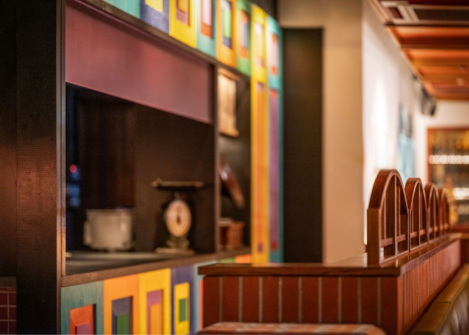 Colorful mosaic wall display with arched wooden bar stools in a stylish restaurant interior.