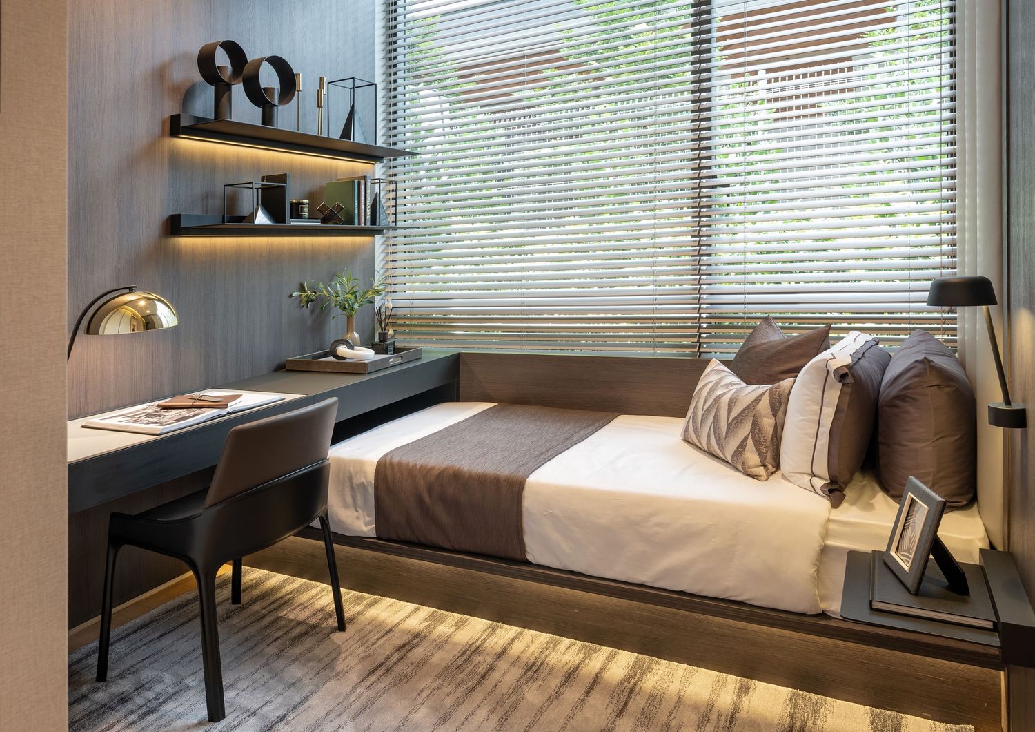 Modern small bedroom with desk, wall shelves, cozy bed, wooden floors, and natural light through blinds.