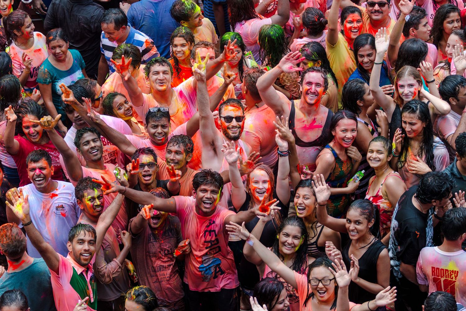 Large crowd of smiling people covered in vibrant colored powder celebrating Holi festival together.