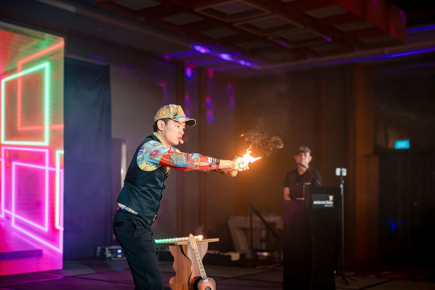 Performer doing fire show with neon light backdrop at indoor event.
