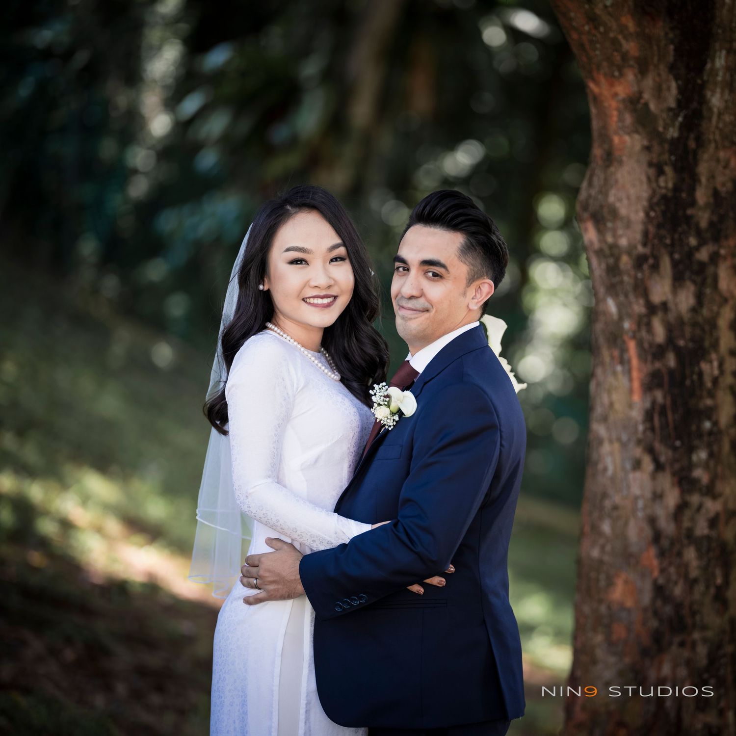 Bride in white gown and groom in navy suit pose together outdoors in a romantic wedding portrait.